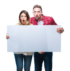 Young couple together holding blank banner over isolated background scared in shock with a surprise face, afraid and excited with fear expression