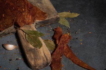 Two pieces of delicious jerky on a wooden board and a tempest background with garlic and spices.