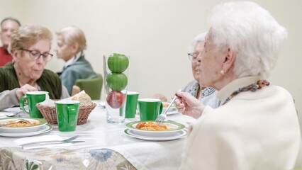 Senior woman eating pasta with friends in nursing home