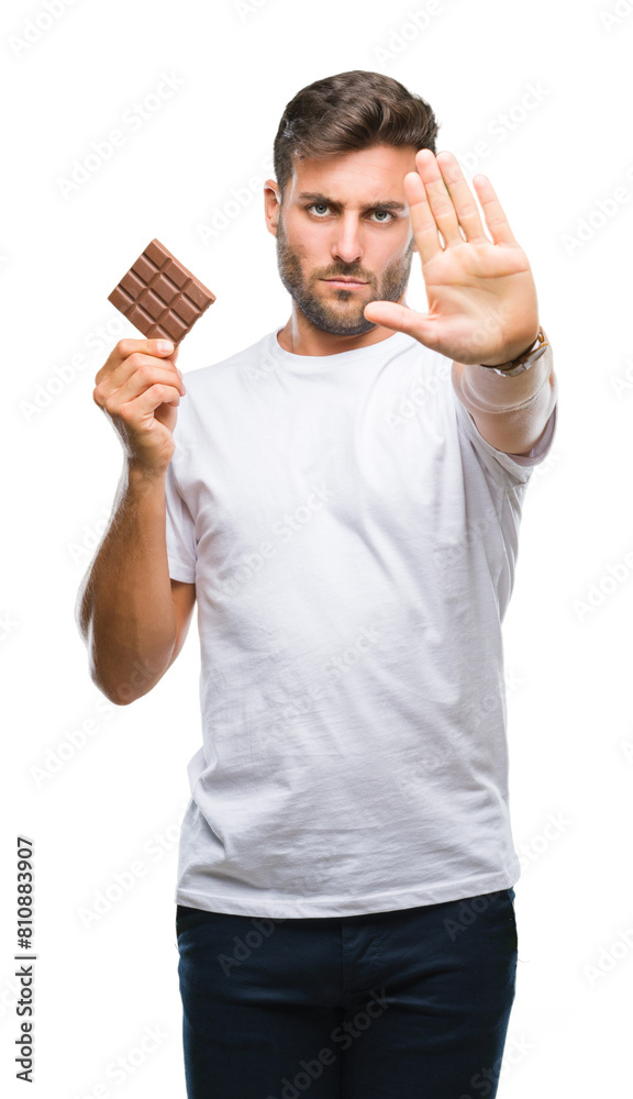 Wall mural Young handsome man eating chocolate bar over isolated background with open hand doing stop sign with serious and confident expression, defense gesture