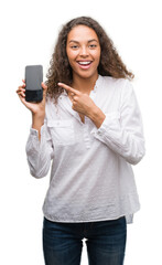 Young hispanic woman using smartphone very happy pointing with hand and finger