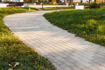 The curved path in the park is paved with gray concrete paving slabs. Selective focus. - Powered by Adobe