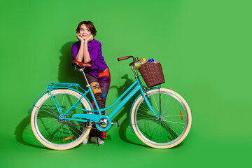 Photo portrait of funny young dreamy woman touch cheeks enjoy summer season driving bicycle isolated on green color background