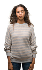Beautiful young hispanic woman wearing stripes sweater with serious expression on face. Simple and natural looking at the camera.