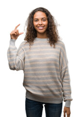 Beautiful young hispanic woman wearing stripes sweater smiling and confident gesturing with hand doing size sign with fingers while looking and the camera. Measure concept.