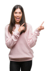 Young beautiful hispanic woman wearing a sweater smiling and looking at the camera pointing with two hands and fingers to the side.