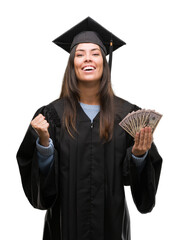 Young hispanic woman wearing graduated uniform holding dollars screaming proud and celebrating...