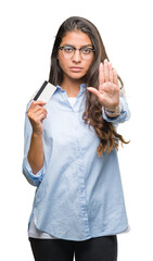 Young arab woman holding credit card over isolated background with open hand doing stop sign with serious and confident expression, defense gesture