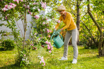 Happy senior woman enjoys watering plants in her garden.	