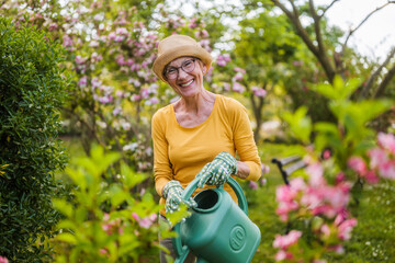 Happy senior woman enjoys watering plants in her garden.	