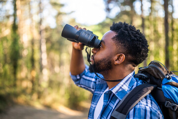 Young man enjoys using binoculars and hiking in nature.	
