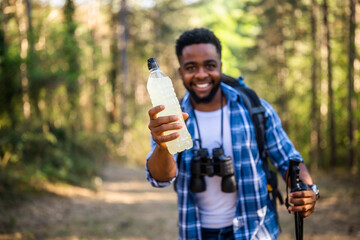 Young man enjoys hiking and drinking energy drink. Focus on bottle.