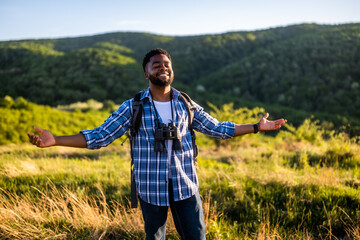 Happy young man hiker with arms raised enjoys in the nature.	