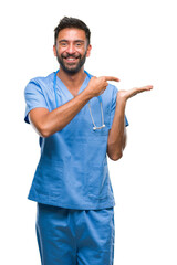 Adult hispanic doctor or surgeon man over isolated background amazed and smiling to the camera while presenting with hand and pointing with finger.