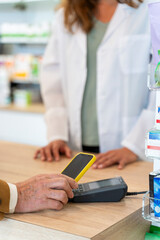 Old man paying with his smartphone at a pharmacy