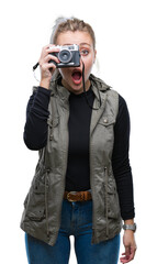 Young blonde woman taking pictures using vintage camera over isolated background scared in shock with a surprise face, afraid and excited with fear expression