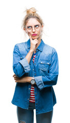 Young beautiful blonde woman wearing glasses over isolated background with hand on chin thinking about question, pensive expression. Smiling with thoughtful face. Doubt concept.