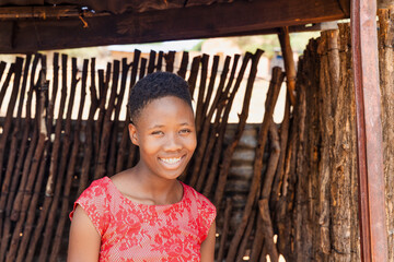 village young african girl with red dress standing i standing at the entrance of the shack,...