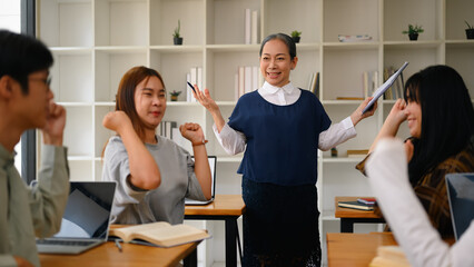 Smiling mature professor with group of students celebrating project success in the classroom