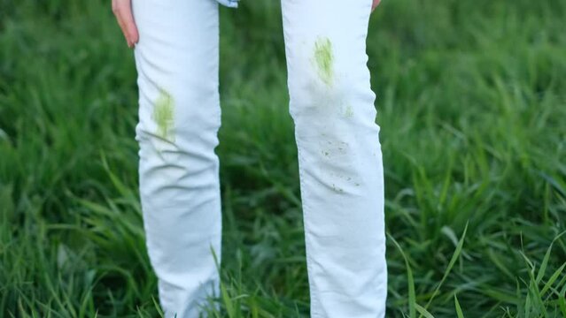 Dirty grass stains on white clothes. An unrecognizable person with green knees on a green background. Spoiled clothes. Daily life dirty stain.outdoors. 