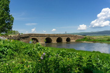 Fototapeta premium Landscape view of mountains, fields, river and ancient bridge of Kushi village. Ktsia, Kushi, Georgia