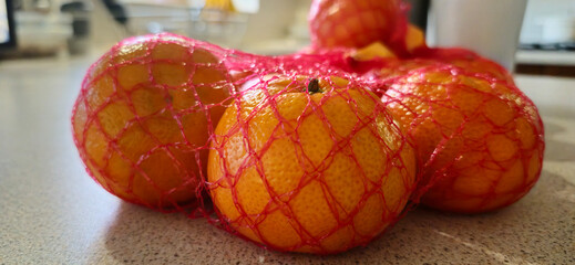 Tangerines in a red mesh bag on a kitchen worktop.