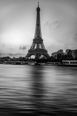 A captivating black and white image capturing the iconic Eiffel Tower standing tall against a cloudy sky, with the Seine River flowing smoothly in the foreground, showcasing Paris timeless beauty
