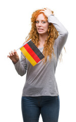 Young redhead woman holding flag of Germany stressed with hand on head, shocked with shame and surprise face, angry and frustrated. Fear and upset for mistake.