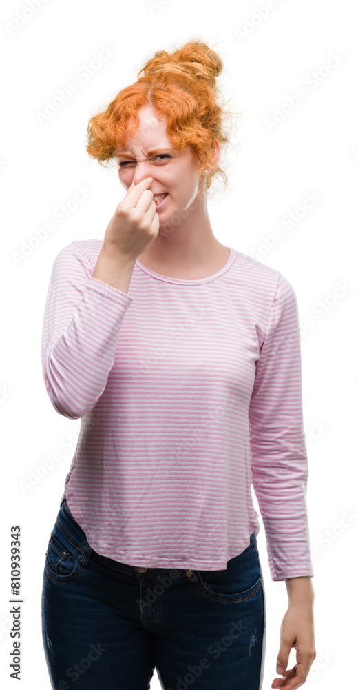 Poster young redhead woman smelling something stinky and disgusting, intolerable smell, holding breath with