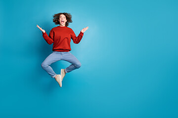 Full length photo of funky impressed guy dressed red pullover jumping high emtpy space isolated blue color background