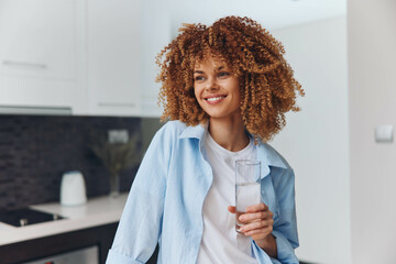 Happy African American woman enjoying a refreshing glass of water in her modern kitchen at home
