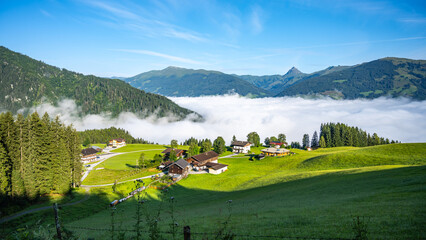 Morning clouds blanket the valley below a serene alpine landscape in Kitzbueheler Alps, with...