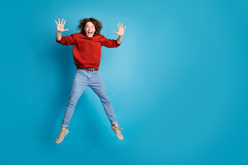 Full length photo of cheerful positive guy dressed red pullover jumping high rising arms emtpy space isolated blue color background