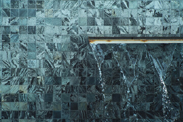 The pouring water from the wall with random design of tiles
