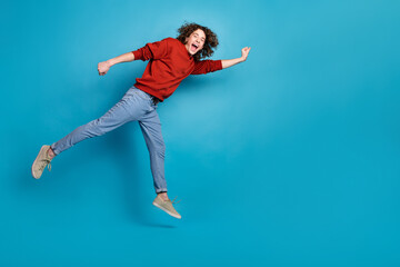 Obraz premium Full length photo of funky cool guy dressed red pullover jumping high hurrying emtpy space isolated blue color background