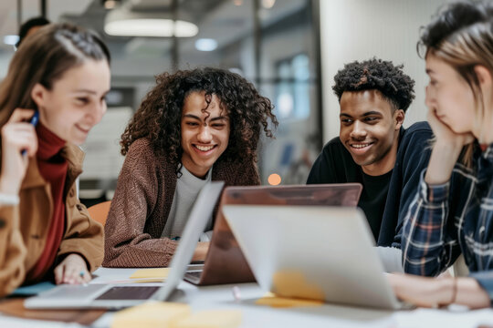 Diverse group of young business people convene in the office for a collaborative meeting, utilizing laptops and tablets for a seminar on startup creativity and education.