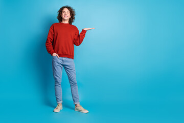 Full length photo of funky cool guy dressed red pullover showing arm emtpy space isolated blue...