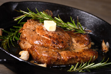 Pork cutlet on the bone in a piece of butter with garlic and rosemary in a frying pan