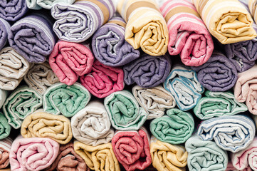 A bunch of colorful towels folded in rows. Rolls of colored rugs lie on a shelf, texture effect