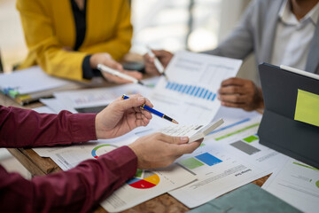 A group of people are sitting around a table with papers and a calculator. They are discussing numbers and graphs