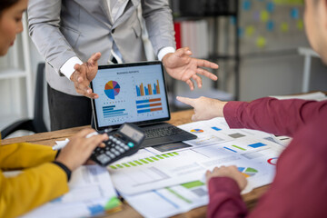 A group of people are looking at a laptop with a pie chart on it. Scene is serious and focused