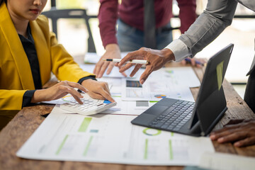 A group of people are working on a project together, with one person pointing at a laptop screen....