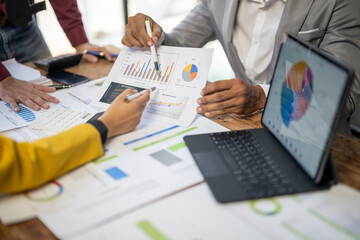 A group of people are looking at graphs and charts on a table. They are discussing the data and making decisions based on the information presented. The atmosphere is serious and focused