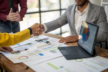 A man shakes hands with another man in a business meeting. The man on the left is wearing a yellow jacket