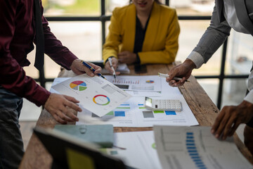 A group of people are working on a project together, with one person holding a calculator and another holding a pen. The atmosphere seems to be focused and collaborative