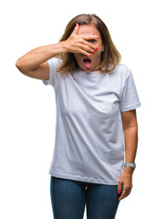 Fototapeta premium Middle age senior hispanic woman over isolated background peeking in shock covering face and eyes with hand, looking through fingers with embarrassed expression.