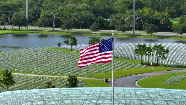 American flag waving over Sarasota National Cemetery with rows of white tomb stones on green grass. Memorial Day concept