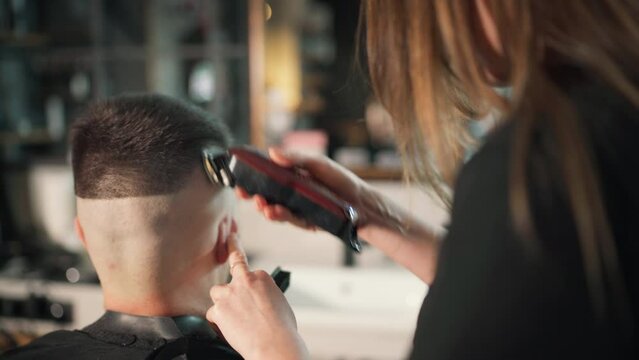 Young female barber making men's undercut haircut hairstyle using Haircut Clipper in Modern style barber shop. Haircare service local small business, cosmetics and personal care industry 4K video