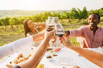 Happy adult friends having fun drinking red wine and eating together with vineyard in background - Multiracial people doing appetizer at summer time in countryside resort - Focus on bottom hands