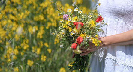 Young caucasian woman in white dress holds wild flowers bouquet on beautiful floral background,...